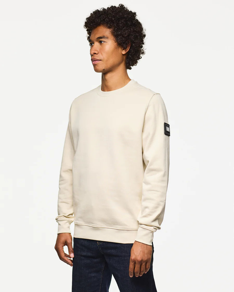 Man wearing a beige sweatshirt with a patch on a white background