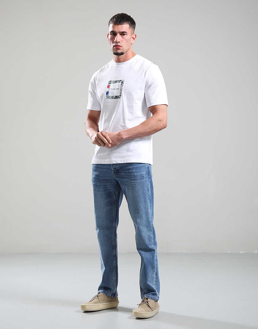 Man wearing a white t-shirt with a logo and blue jeans on a gray background