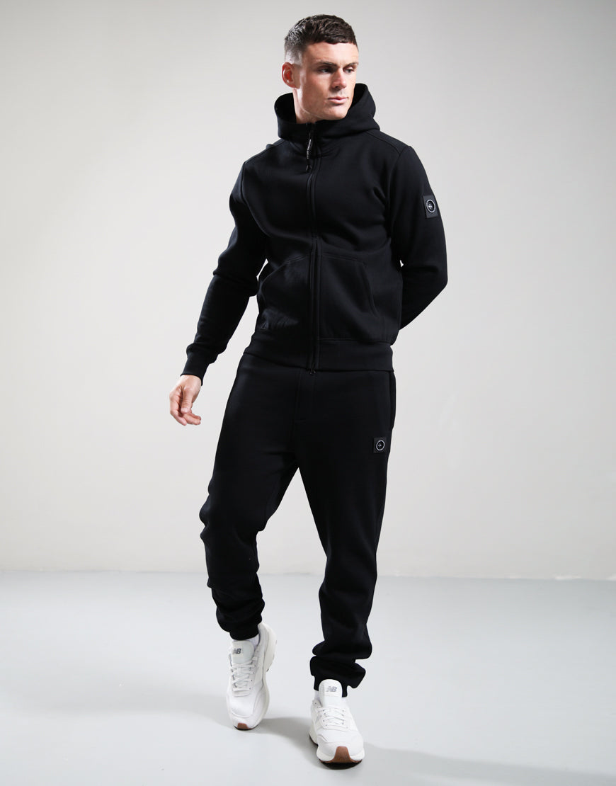 Man wearing a black tracksuit with a brand logo on a gray background