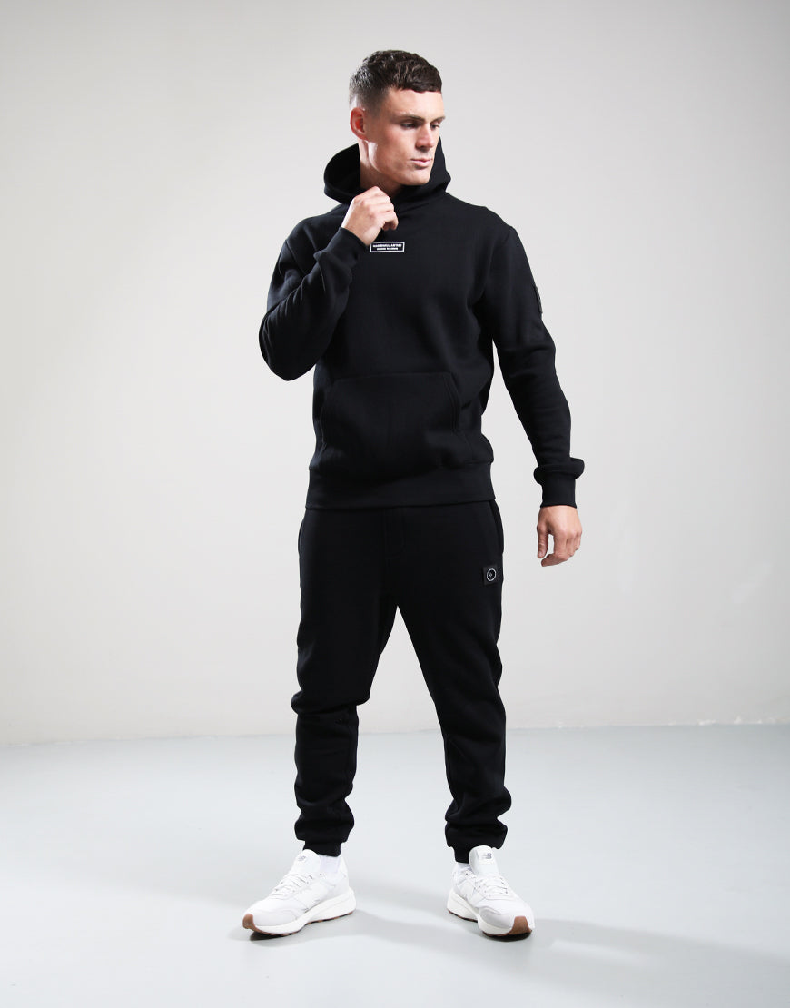 Man wearing a black tracksuit with a hood on a gray background