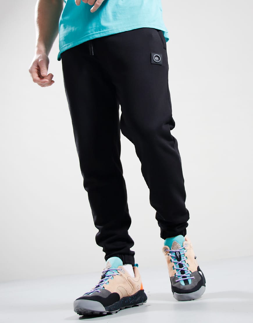 Person wearing black jogger pants and colorful sneakers on a light gray background