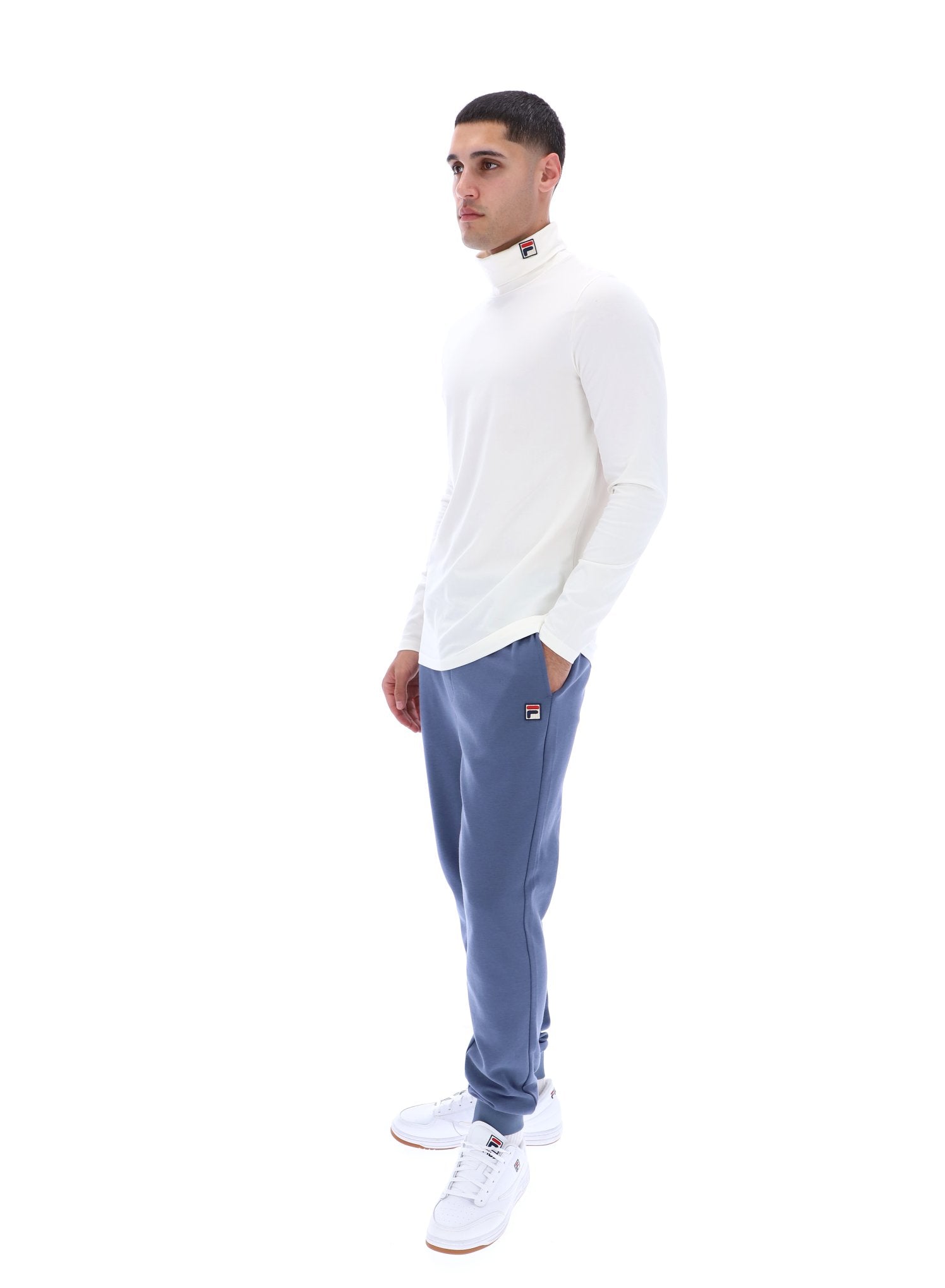 Man wearing a white long-sleeve shirt and blue tracksuit pants on a white background