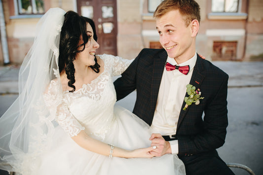 Couple in wedding attire sitting outdoors on a street.
