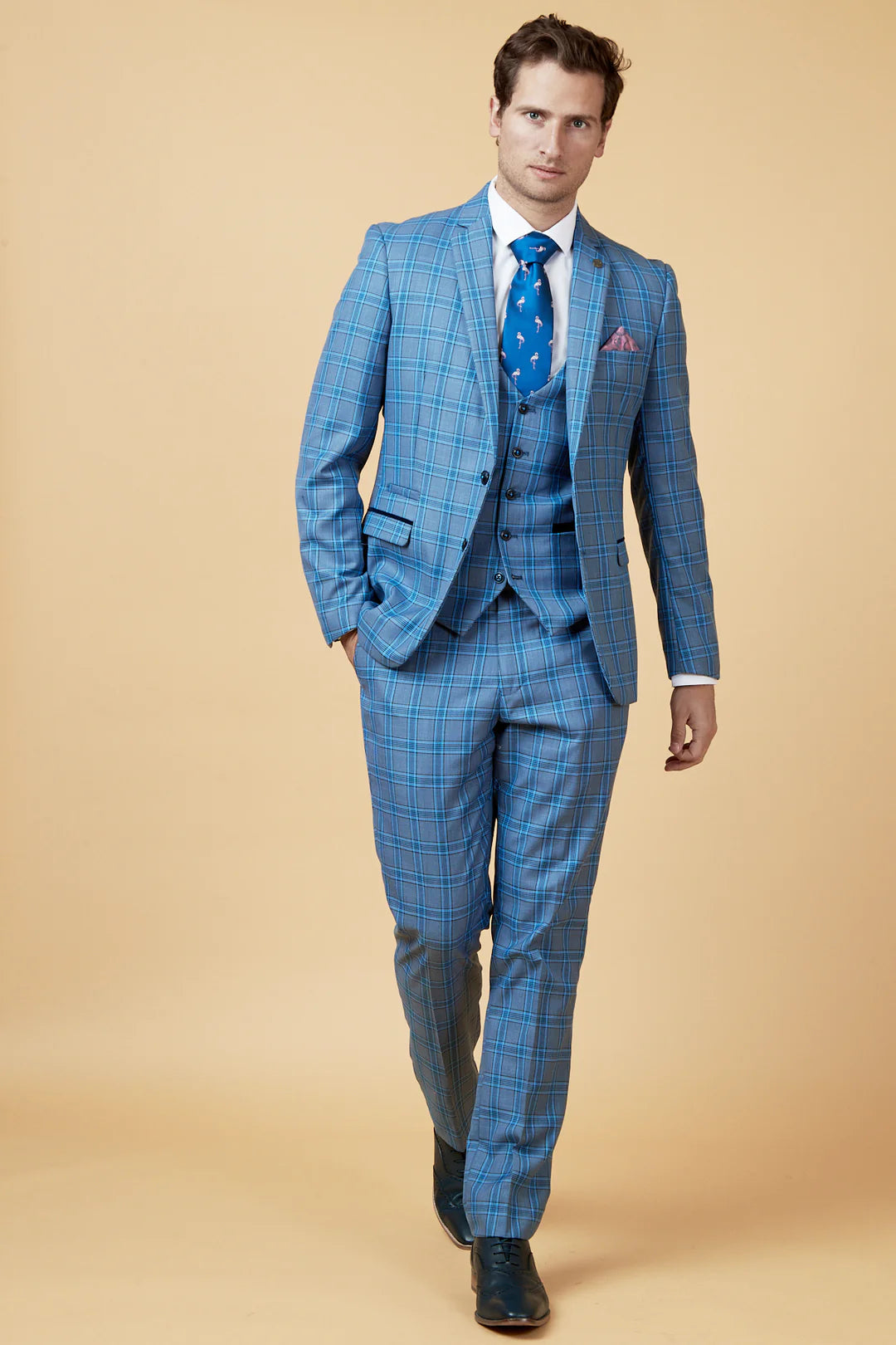 Man wearing a blue checkered suit with a matching tie against a beige background