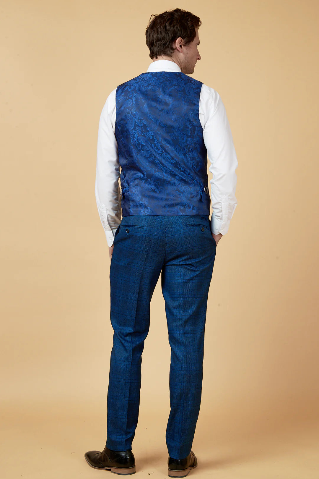 Man wearing a blue vest and pants with a white shirt on a beige background