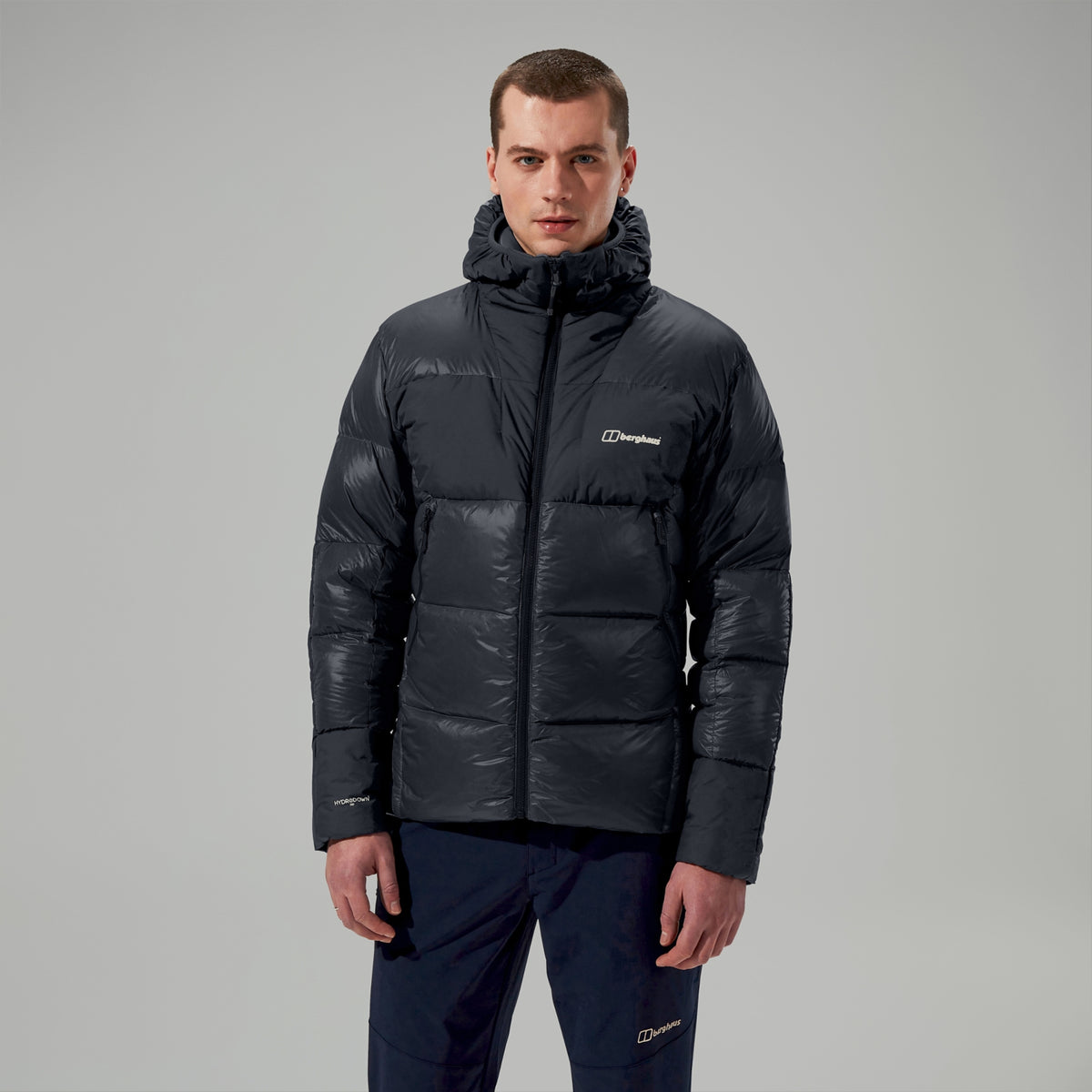 Man wearing a black puffer jacket with a brand logo on a gray background