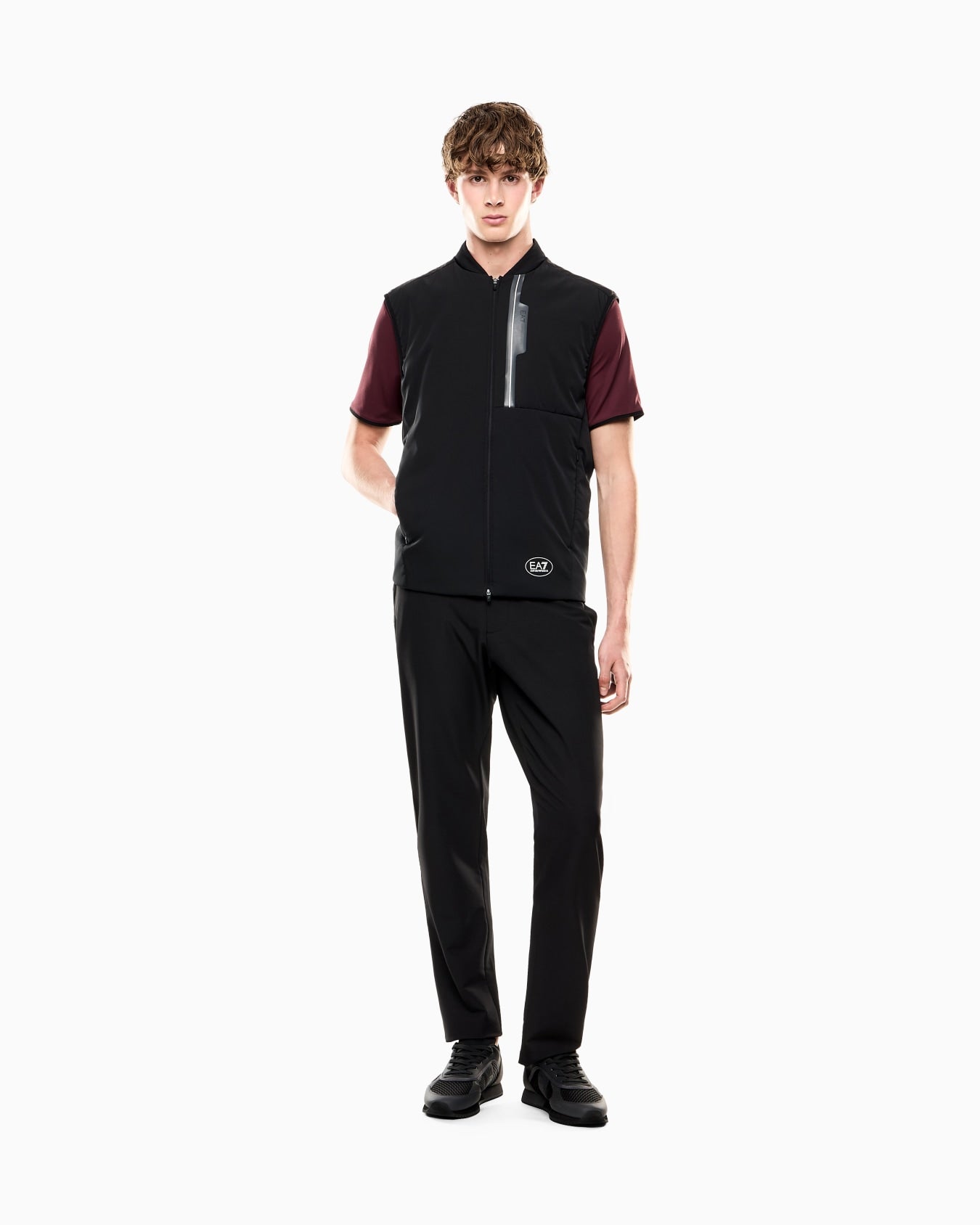 Person wearing a black vest with maroon accents and black pants on a white background