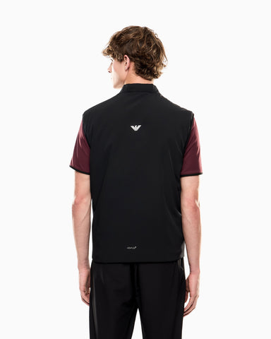 Person wearing a black and maroon polo shirt with a logo on the back, standing against a white background.