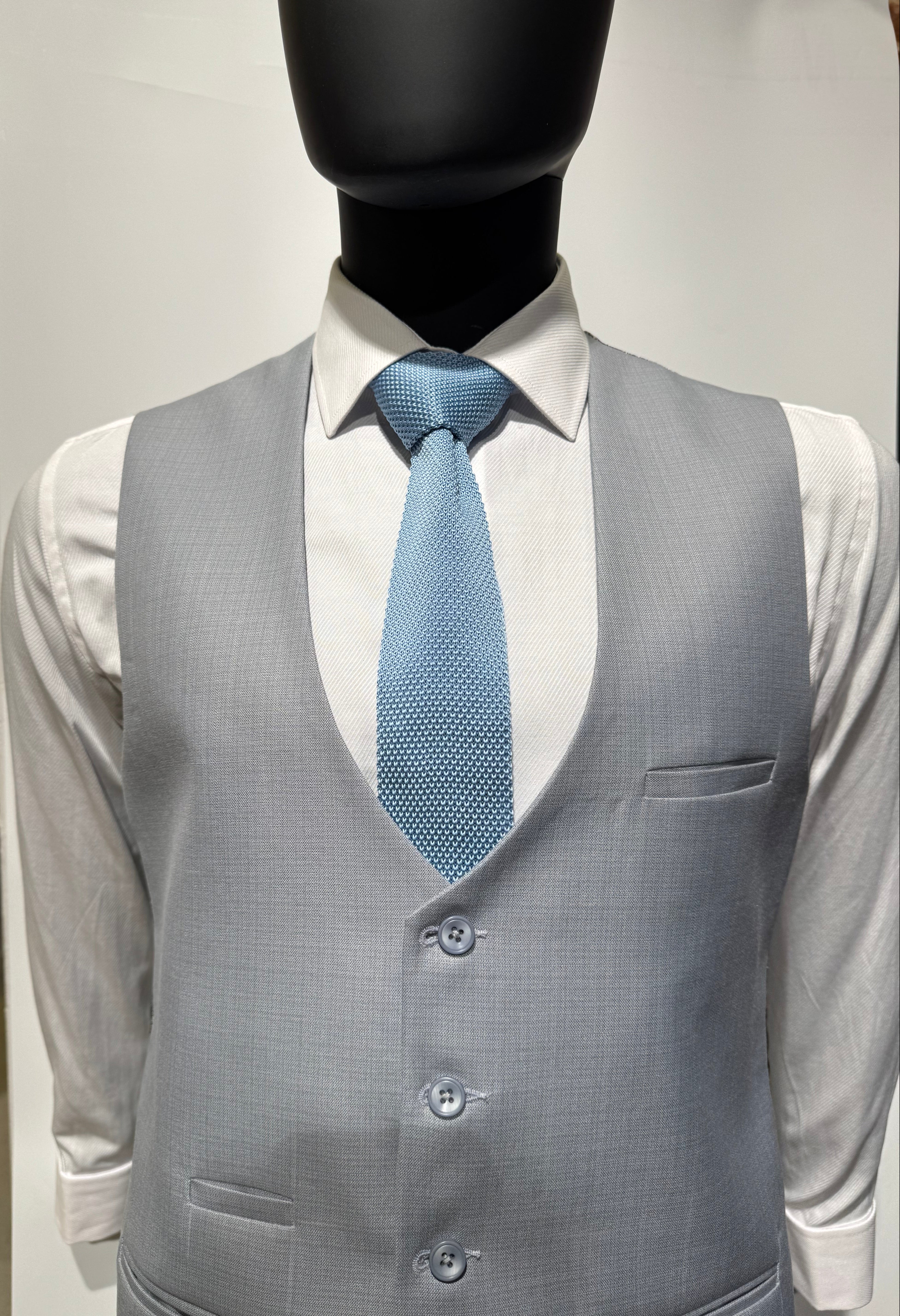 Gray suit jacket with a blue tie being ironed on a white background