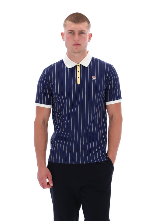 Man wearing a navy pinstripe polo shirt with a white collar and yellow accents on a white background