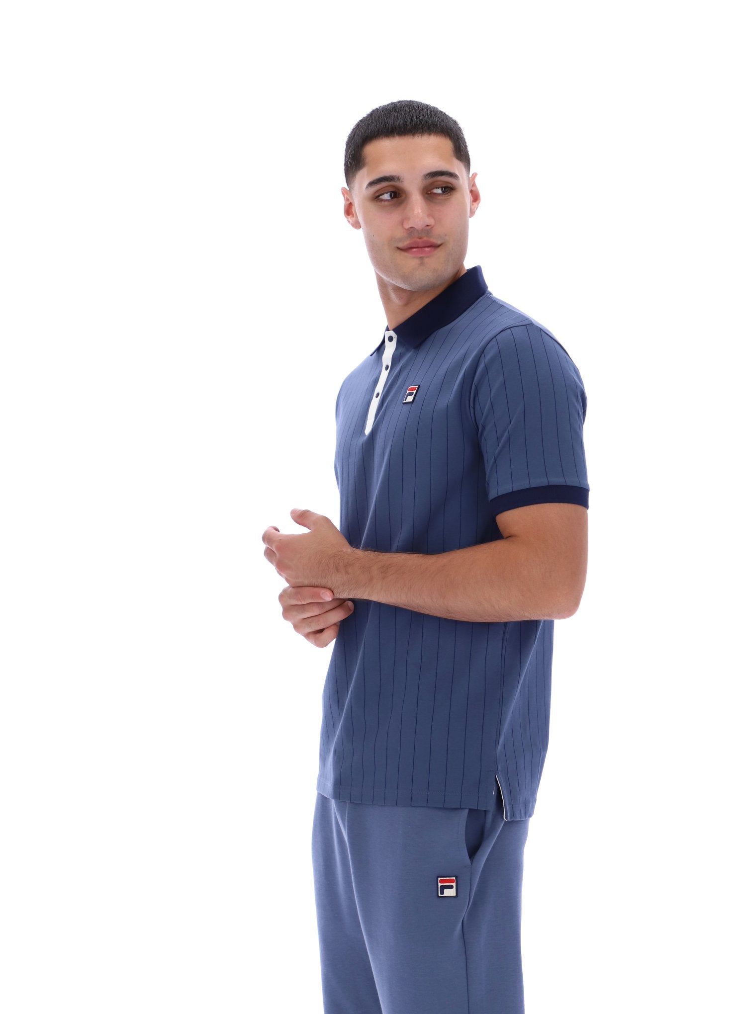 Man wearing a blue polo shirt and pants with a visible brand logo on a white background