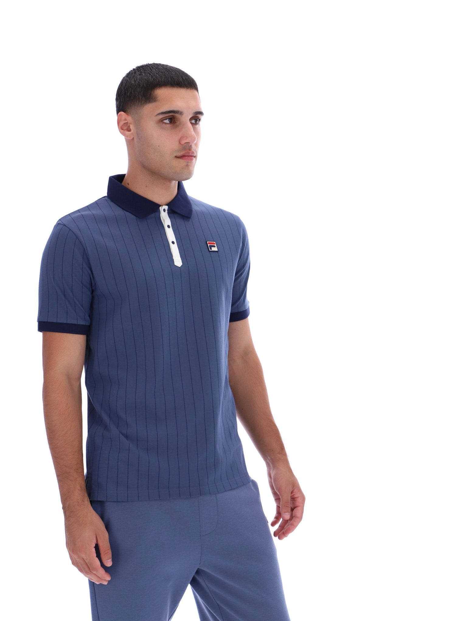 Man wearing a blue ribbed polo shirt with a small logo on a white background