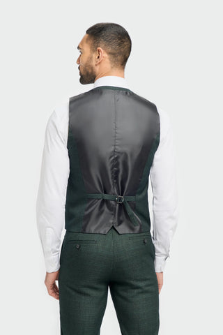 Man wearing a dark green vest and green pants on a plain background