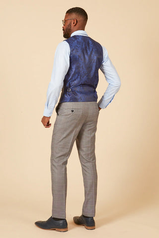 Man wearing a blue vest and gray pants against a beige background