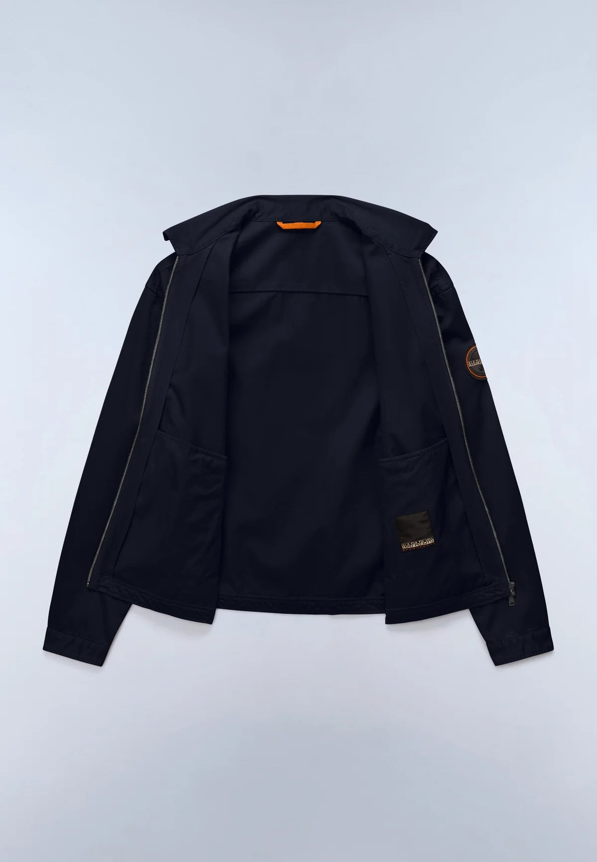 A black zip-up jacket with a high collar, laid flat against a light gray background. It features a small orange accent at the inner collar and a circular patch on the left sleeve.