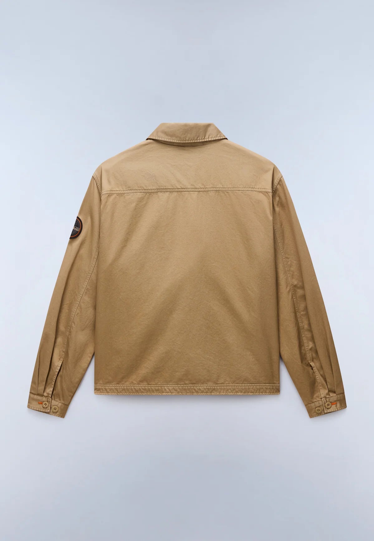 A tan utility jacket shown from the back, featuring a collar, long sleeves, and a small circular patch on the left sleeve, photographed against a light gray background.