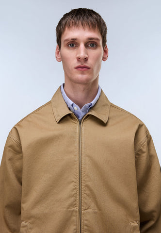 Man wearing a beige jacket over a light blue shirt on a plain background