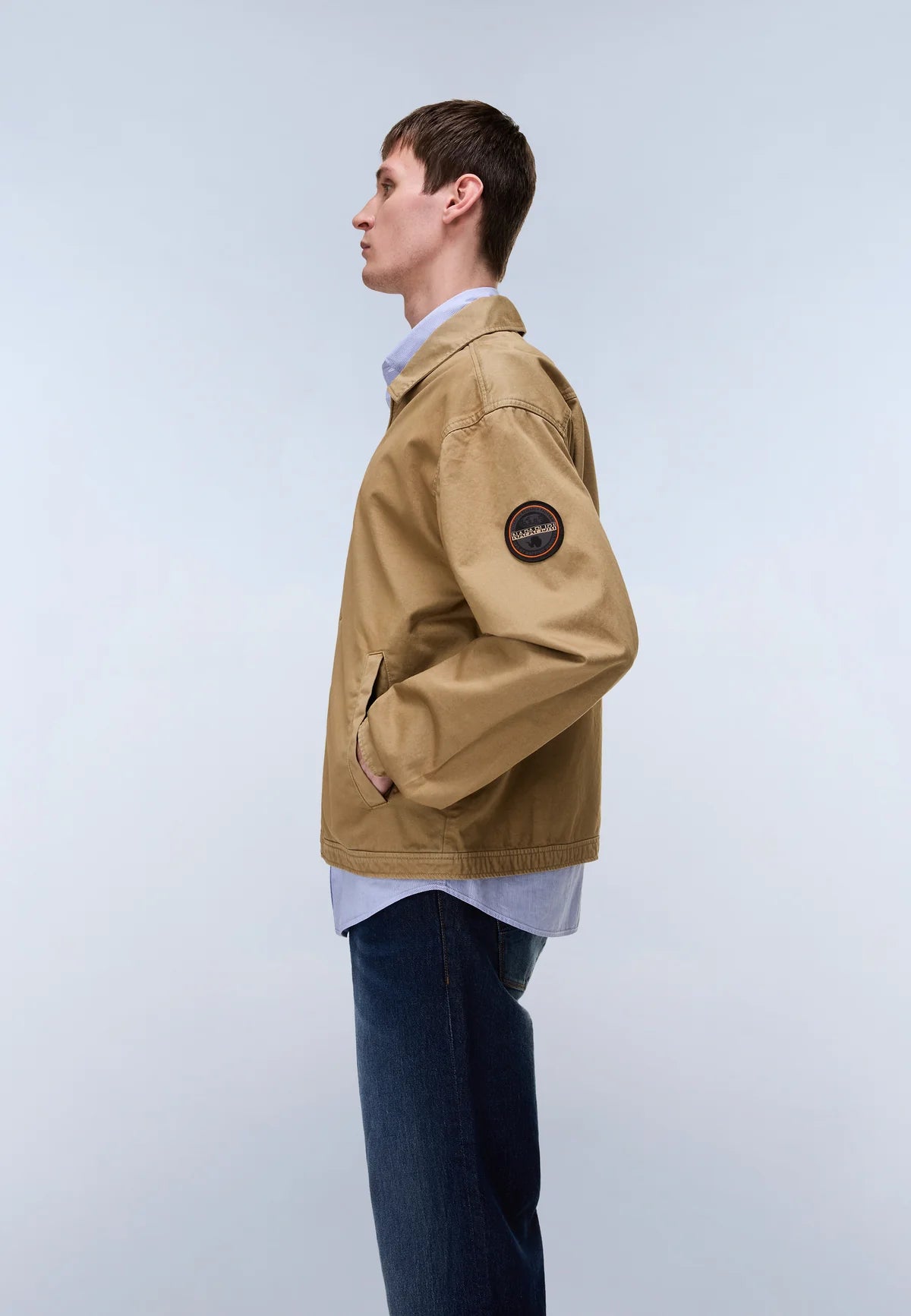 Person wearing a beige jacket with a logo on a light gray background
