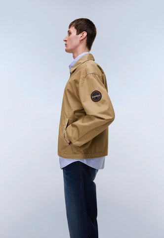 Person wearing a beige jacket with a logo on a light gray background