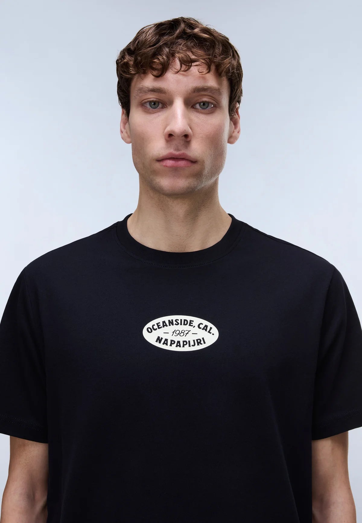 Person wearing a black t-shirt with a logo on a plain background