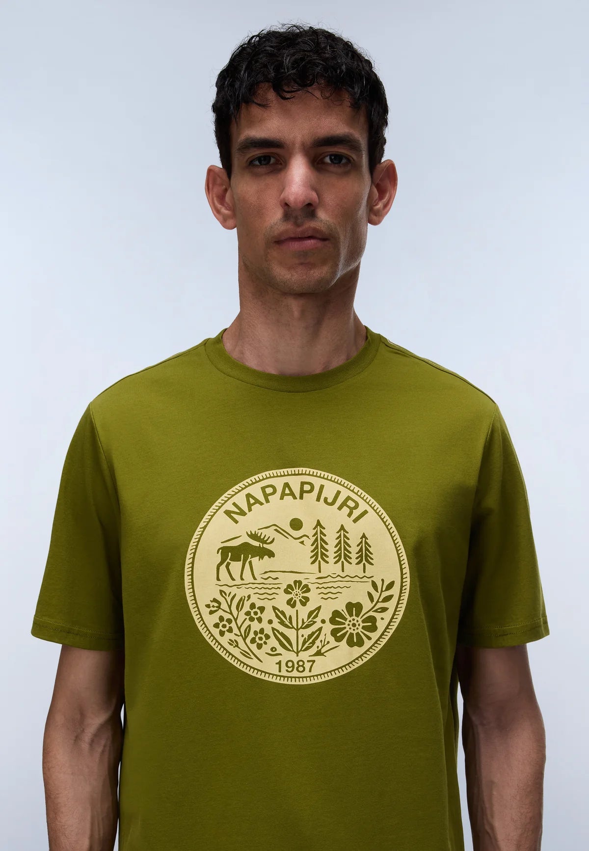 Man wearing a green t-shirt with a logo and text on a light gray background