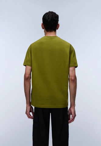 A man viewed from behind wearing a short-sleeve olive green t-shirt and black pants, standing against a light gray studio background.