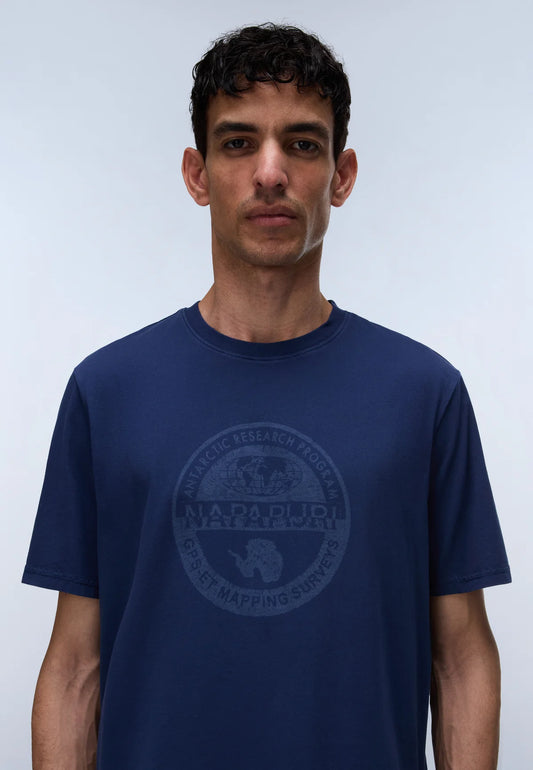 A man wearing a navy blue crewneck t-shirt with a dark gray circular graphic on the chest featuring a polar bear and the text 'NARNUPIU ARCTIC RESEARCH FOUNDATION' and 'ARCTIC MAPPING SURVIVOR'.