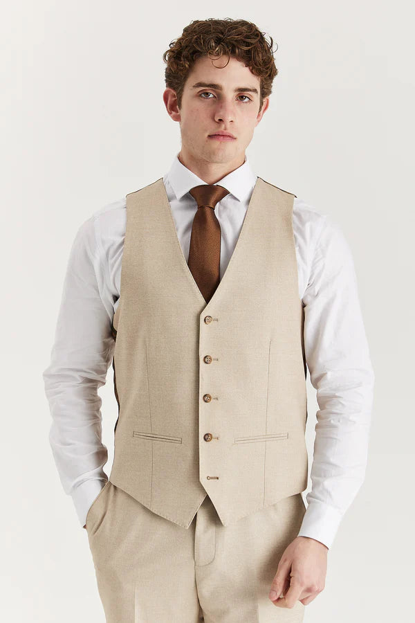 Man wearing a beige vest over a white shirt with a brown tie on a light gray background