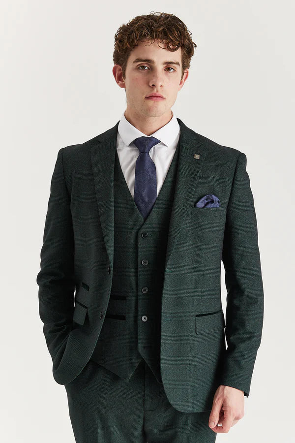Man wearing a dark green suit with a white shirt and blue tie on a light gray background