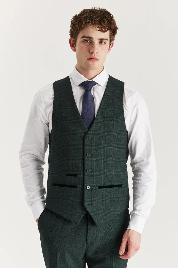 Man wearing a green vest over a white shirt with a blue tie on a light gray background