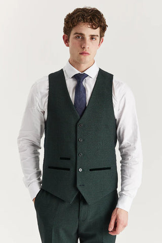 Man wearing a green vest over a white shirt with a blue tie on a light gray background
