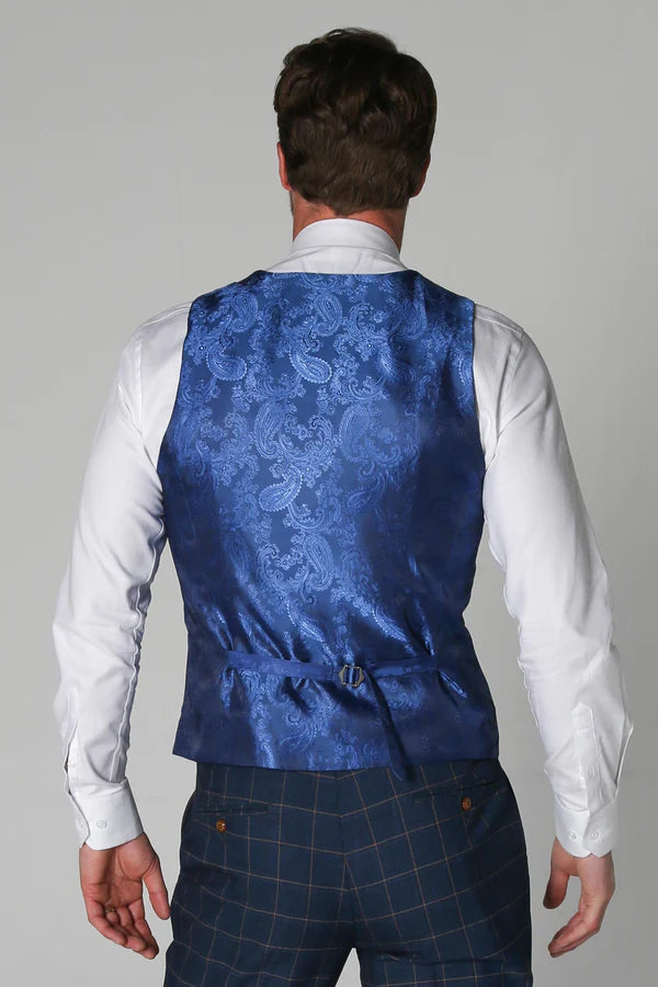 Man wearing a blue patterned vest over a white shirt and dark plaid pants on a gray background