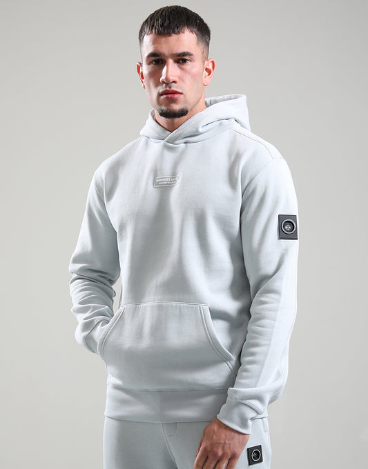 Man wearing a light gray hoodie with brand logos on a plain background