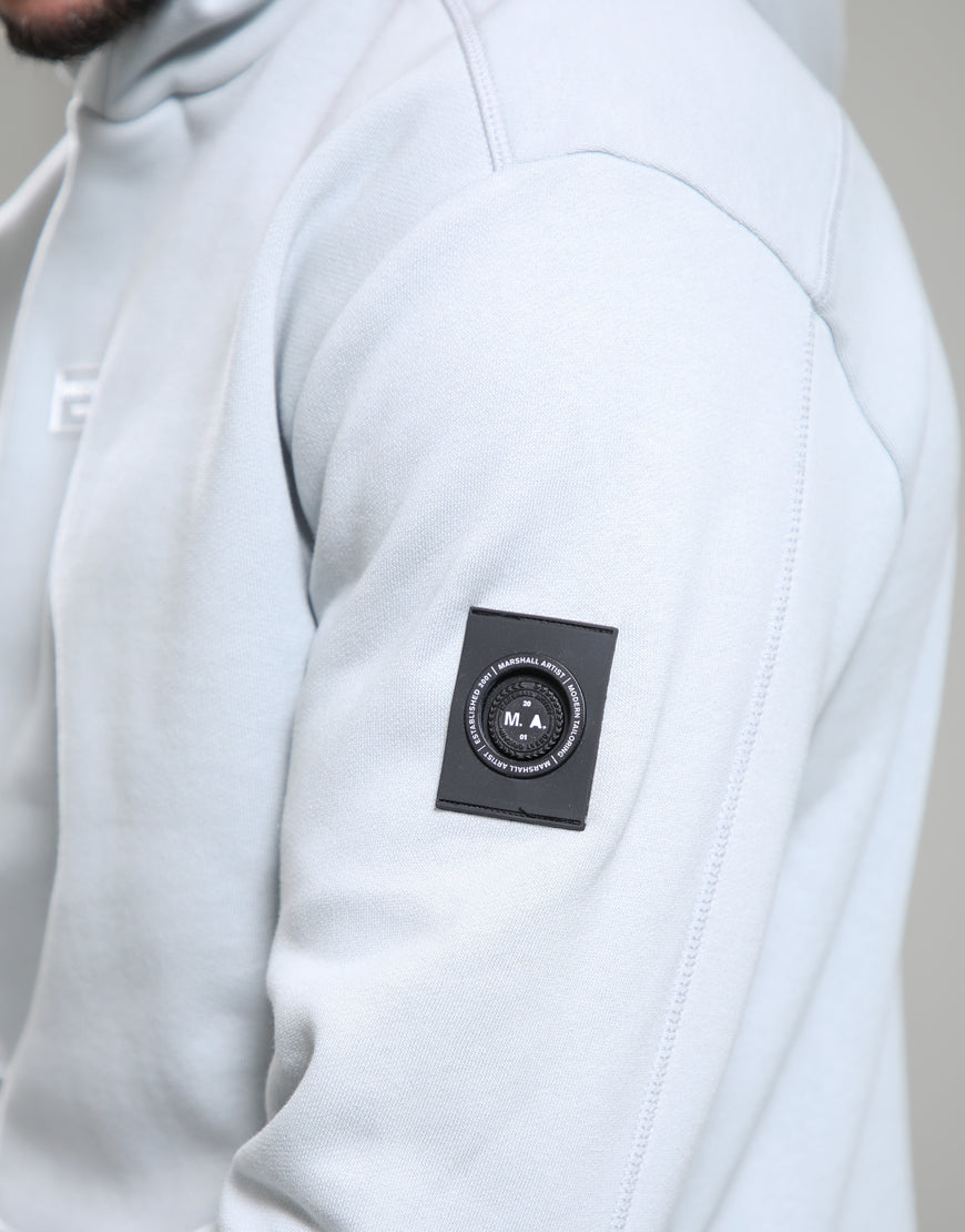Close-up of a light gray hoodie with a brand logo on the sleeve against a neutral background