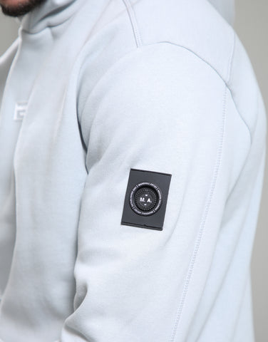 Close-up of a light gray hoodie with a brand logo on the sleeve against a neutral background