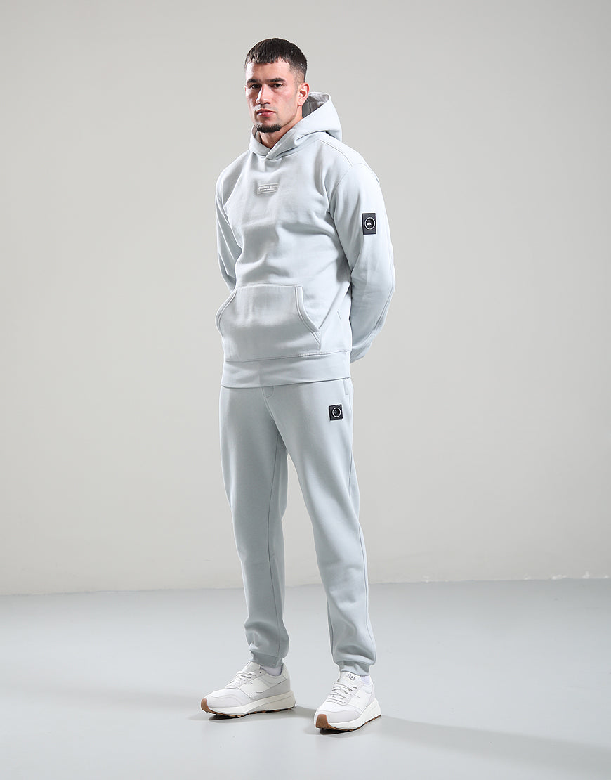 Man wearing a light gray hoodie and pants with a logo on a plain background