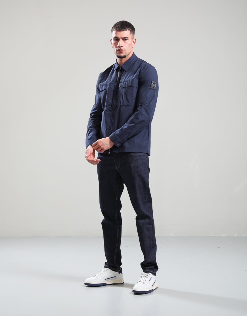 Man wearing a navy jacket and jeans standing against a plain background