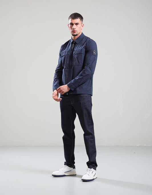 Man wearing a navy jacket and jeans standing against a plain background