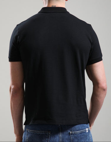 A man viewed from behind wearing a plain black short-sleeve polo shirt and blue jeans, standing against a neutral light gray studio background.
