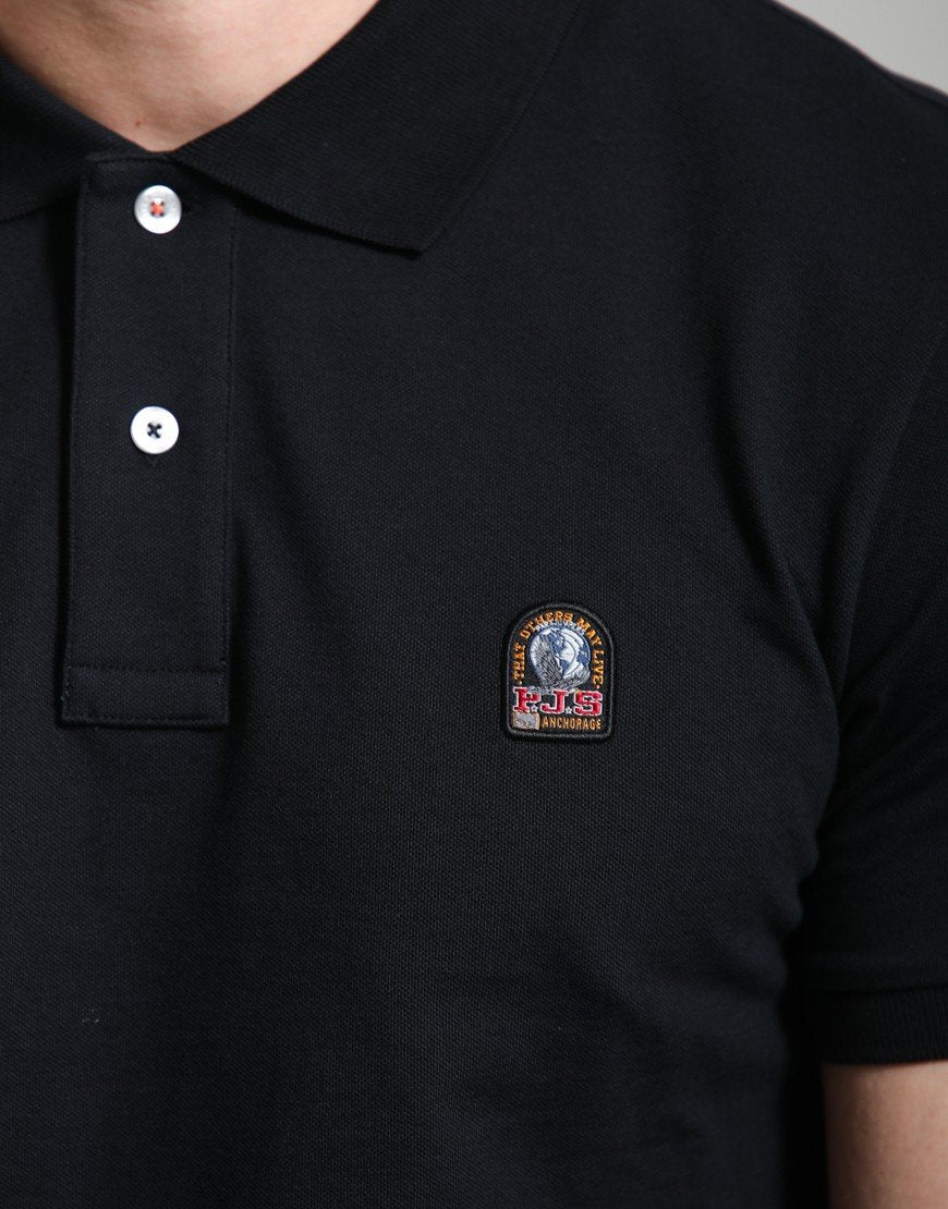 Close-up of a black short-sleeve polo shirt worn by a model, featuring a small embroidered Kith x Cactus Jack logo patch on the left chest.
